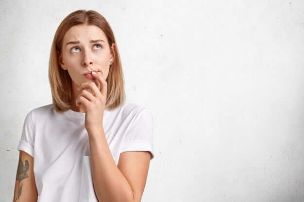 cute-pensive-young-woman-tries-gather-with-thoughts-looks-upwards-while-thinks-doubts-mind-has-tattooed-arm-dressed-casual-white-t-shirt-isolated-studio-wall_273609-16929